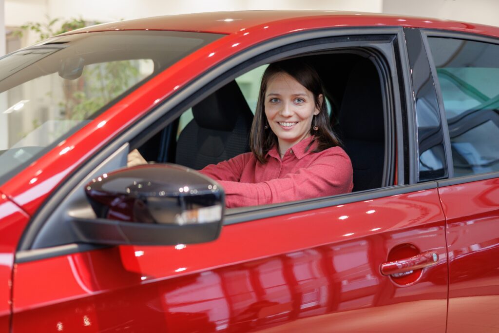 happy European woman in a red car at a car dealership, buying a car on credit or trade in